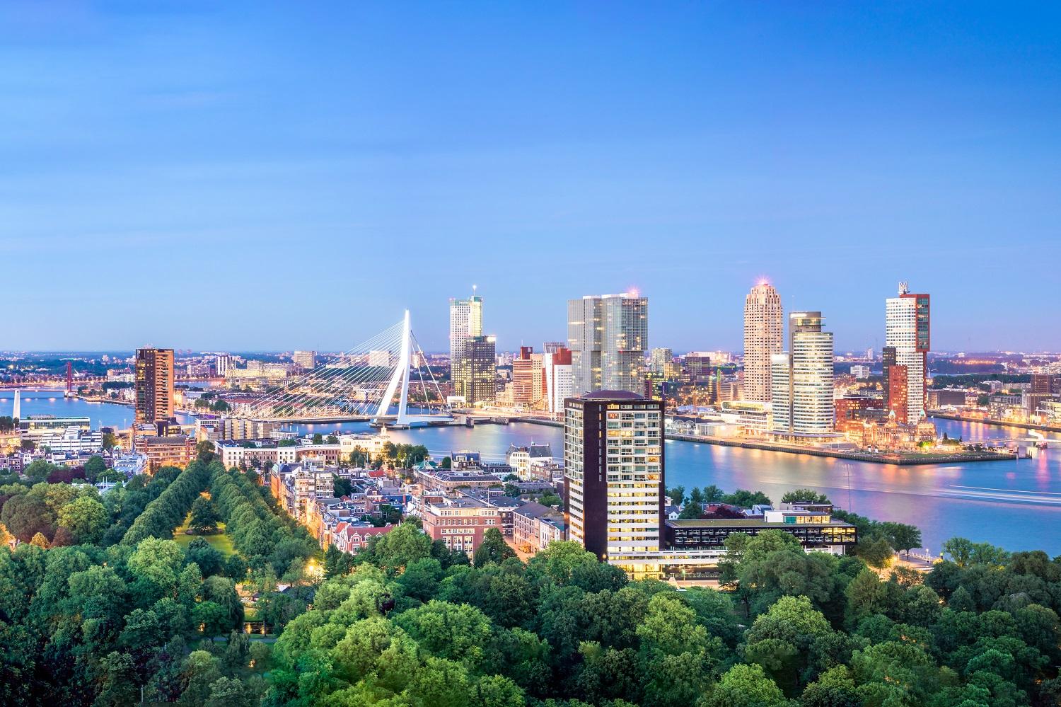 An aerial view of the city of Rotterdam with the Maas river, the Erasmus bridge, high buildings and greenery.