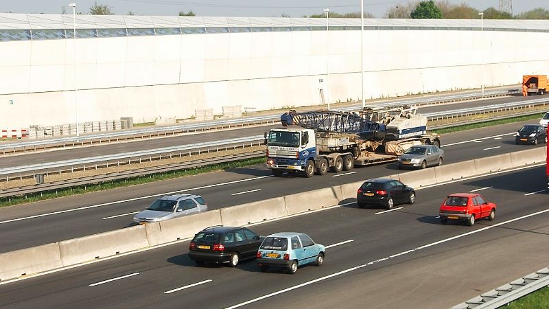 A motorway with cars and a white noise barrier.