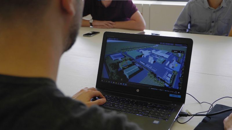 You are looking over the shoulder of a man who is viewing a visualisation of a terrain on his laptop.