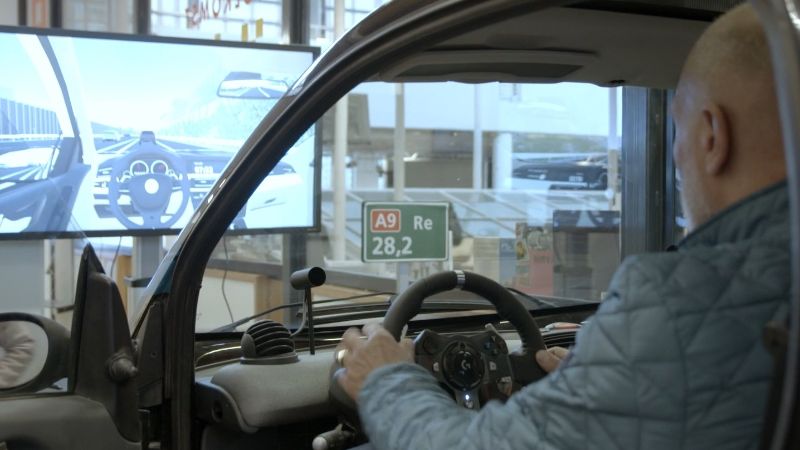 A man in the driving simulator. In front of him is a screen showing the image he sees.