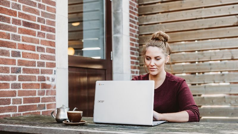 A photo of a woman typing behind her laptop in a garden.