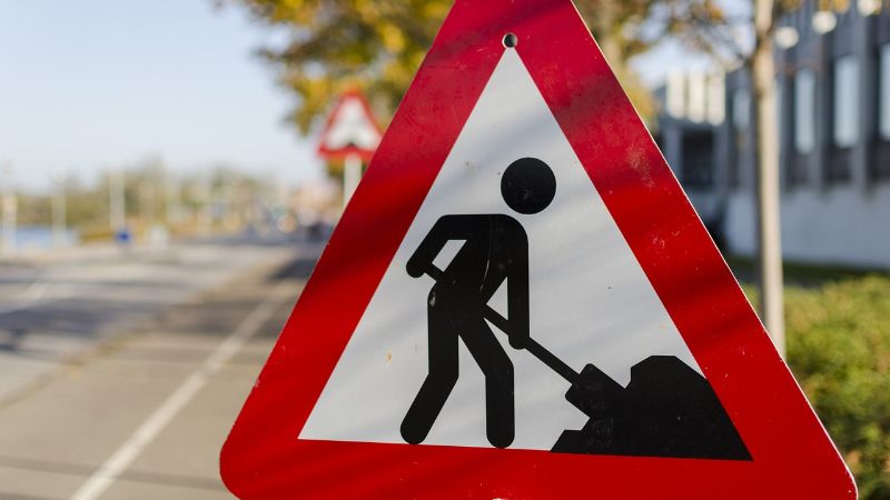 A triangular traffic sign with a red border. The sign says that there are road works.