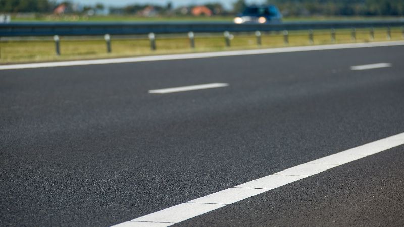 Een foto van het asfalt met witte lijnen van een snelweg.