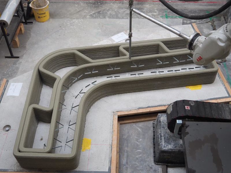 Foto van een 3D betonprinter in een fabriek. De 3D betonprinter is bezig.