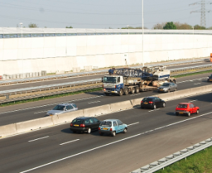 A motorway with cars and a white noise barrier.