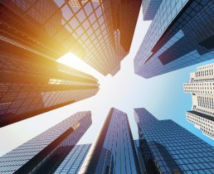 A photo taken from the ground up in the air. You can see the sun and buildings. 