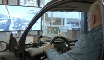 A man in the driving simulator. In front of him is a screen showing the image he sees.