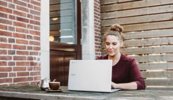 A photo of a woman typing behind her laptop in a garden.