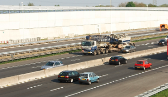 A motorway with cars and a white noise barrier.