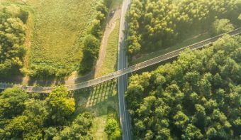 An aerial view of a road and a cycle bridge in a green setting.